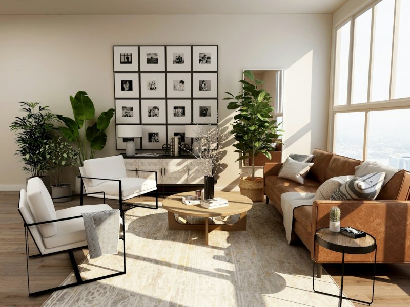 Bright living room with a tan leather sofa, white armchairs, large plants and a gallery wall