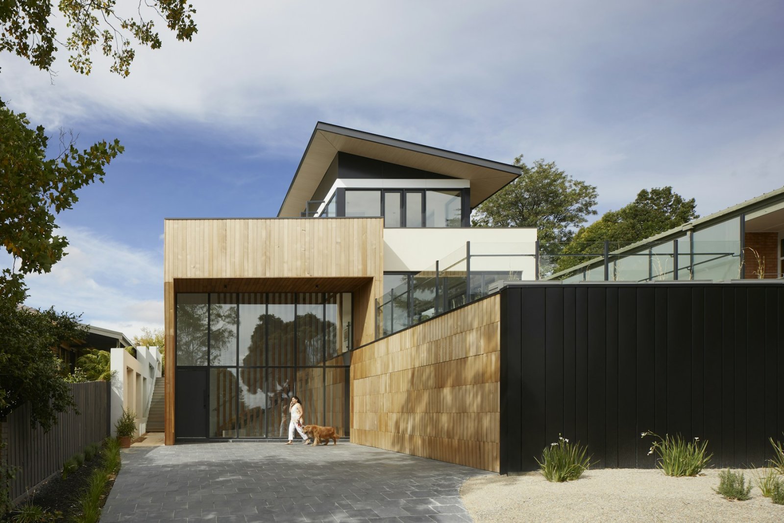 Timber-clad entrance of a contemporary home with a glazed facade and gravel drive